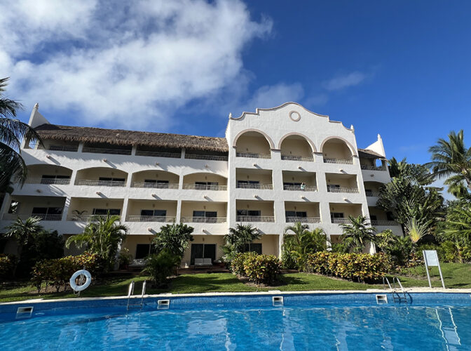 White hacienda-style hotel building and turquoise pool with blue sky at Excellence Riviera Cancun.