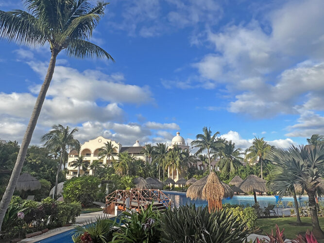 Palm trees and foliage in front of a hacienda-style building at Excellence Riviera Cancun.