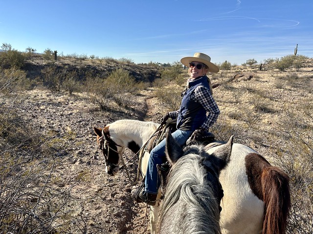 Wrangler Sera Skellenger riding on her paint horse. She's looking back at the photographer with a big smile, wearing a wide brimmed, straw cowboy hat. 