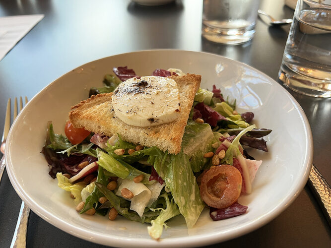 Baked goat cheese on top of salad greens on a restaurant plate.