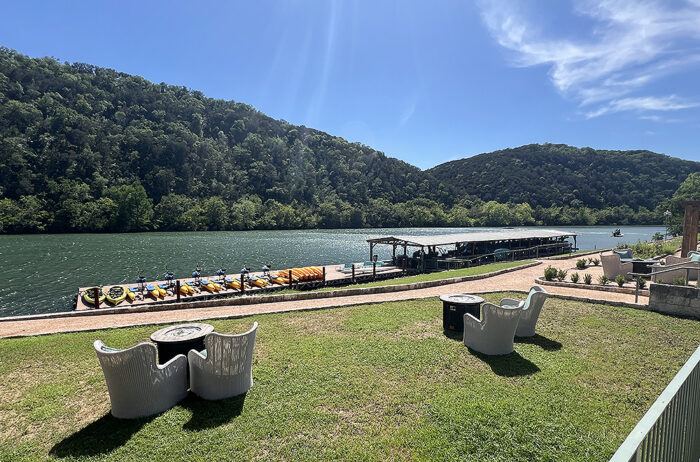 Grassy lawn with seating areas in front of river with hydrobikes and stand-up paddleboards