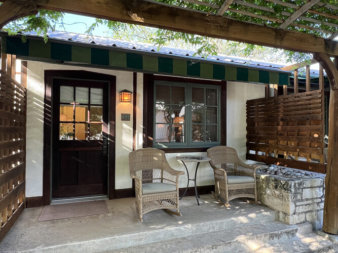 Wicker chairs on a porch in front of a rustic looking hotel room.