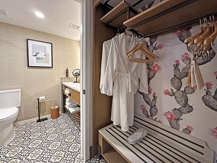 A closet niche decorated with cactus print wallpaper leads to a spacious bathroom with decorative tile flooring