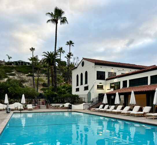 Swimming pool next to a Spanish-Mediterranean bathhouse and palm trees