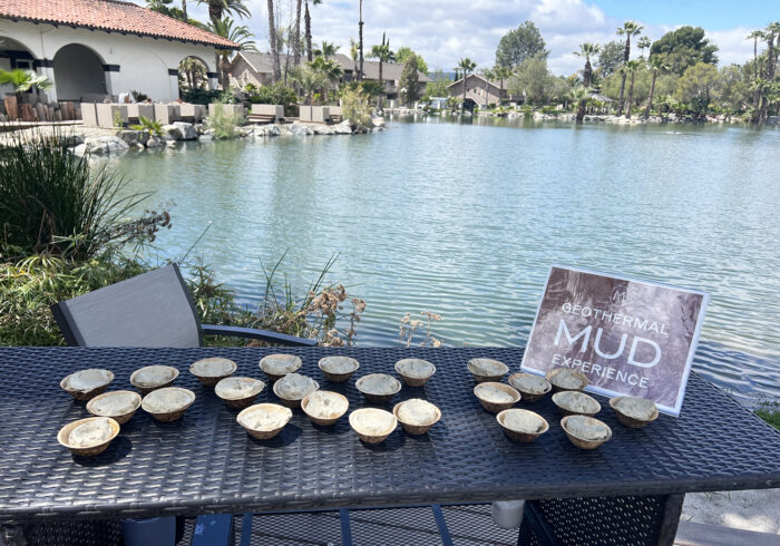 Ramekins of mud on a wicker table in front of a lake with palm trees