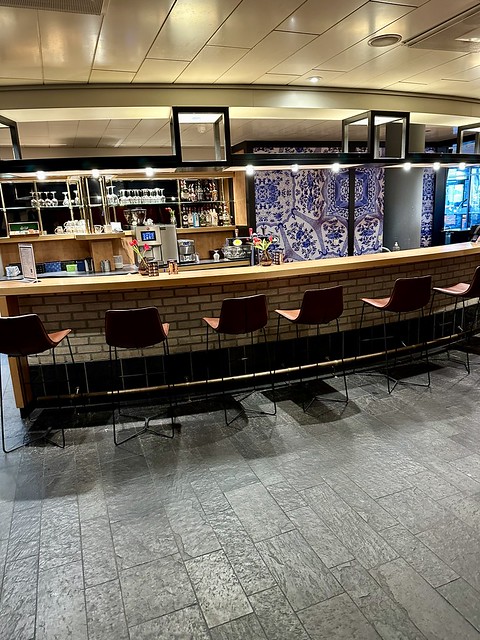 Bar with liquor bottles behind counter and stemware. Five bar stools are below the hotel bar counter. 