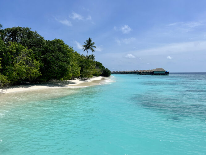 Aqua seawater against white sand beach and overwater bungalows.