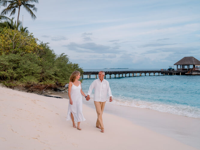 Couple holding hands walking on a white-sand beach.