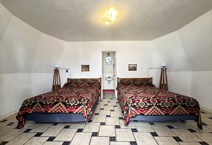 A small circular room features two beds with rustic hickory furniture and a door to a small bathroom