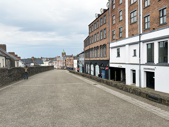 The wide ancient stone wall of Derry runs between rows of homes brick buildings. 