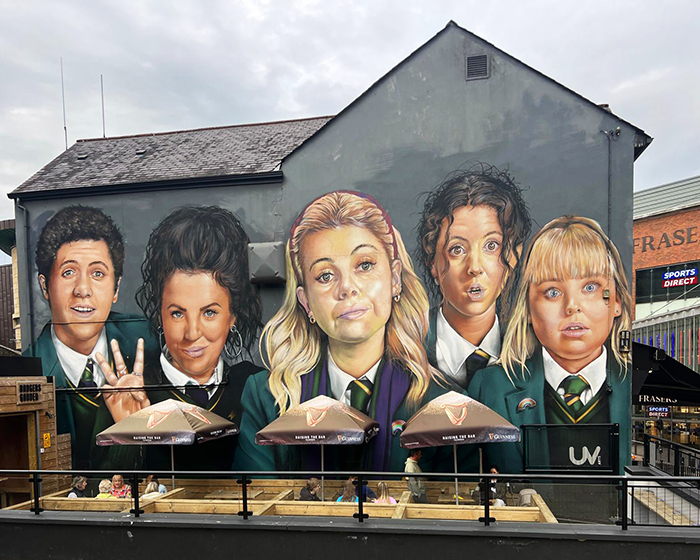 A mural of five teenagers from Derry Girls is on the side of a building