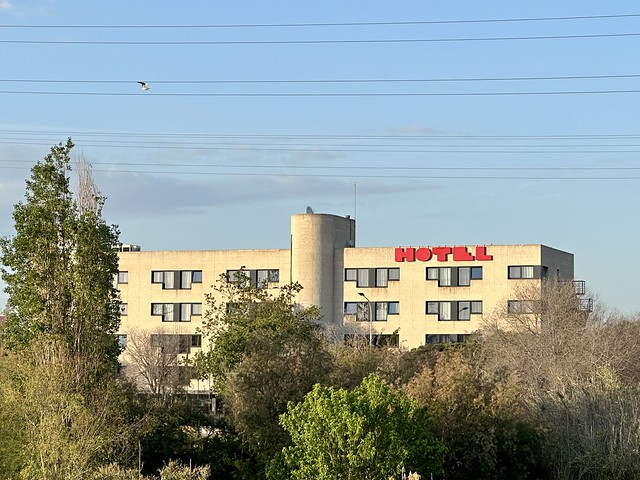 4-story Hotel Alfa Aeropuerto, white building with cement pillar separating the hotel. Red letters spell out hotel on the top, right of property. 