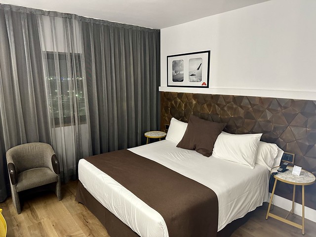 King hotel room with white comforter, brown square pillow and brown throw on bottom of bed. 