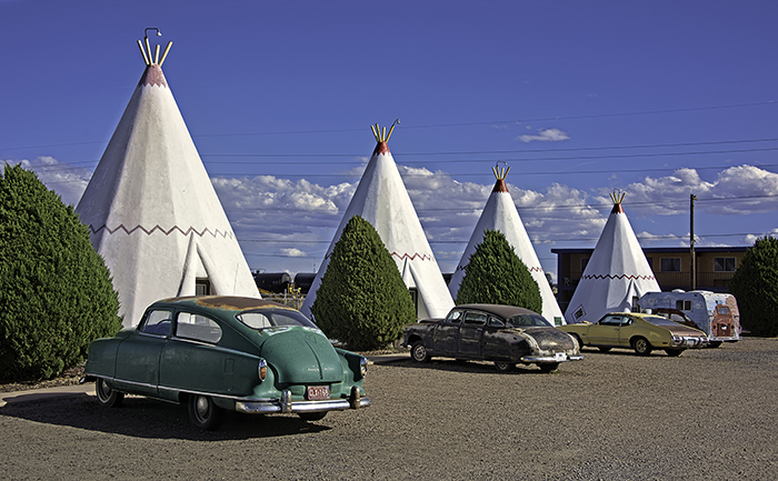 Vintage cars sit in front of a row of concrete tipis that make up Wigwam Village #6