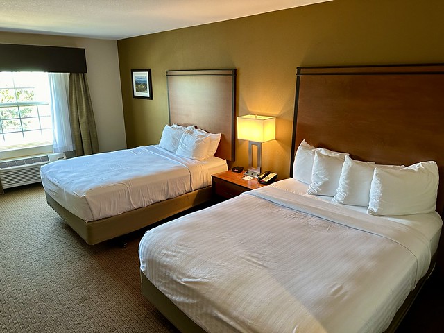 Double queen hotel room with white sheets and 4 white pillows on each bed. A bedside lamp, with phone charging plug-ins, was between the beds. 