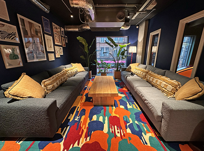 A funky private seating area feature two long gray sofa, plants, and a boldly colored and patterned carpet.