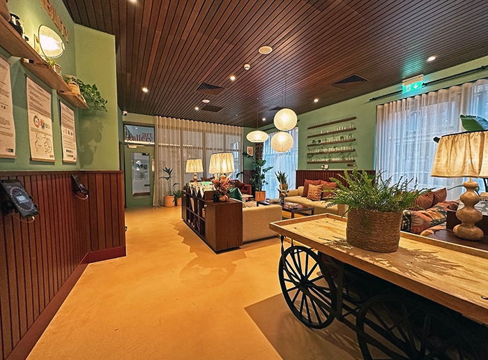 A sitting room features soft green walls, wood wainscot and ceilings, and lots of natural greenery