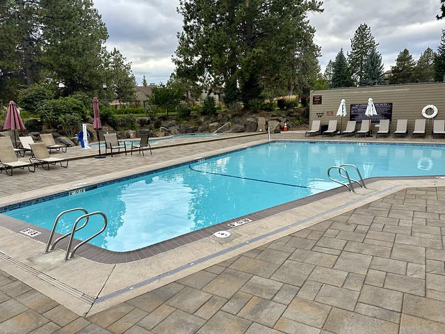 One of two outdoor swimming pools on property. This rectangular pool had 8 chaise lounges and 2 cloth umbrellas at the deep end of the pool. Between the pool and the hot tub were more chaise lounges and 2 cloth umbrellas that were not fully opened. The fenced pool was surrounded by mature trees. 