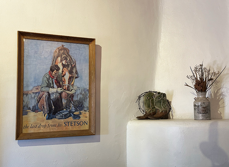 Lon Megargee's Last Drop painting hangs next to a display of cowboy boots and dried desert plants