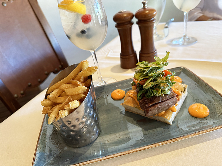 An open-face steak sandwich and fries on a plate with a cocktail