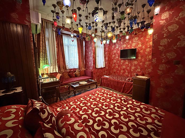 Red guest room with red linens and upholstered furniture and dozens of hanging glass ceiling lamps