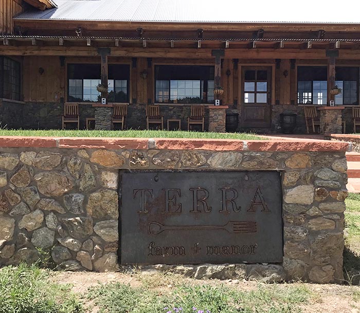 Set in a stone wall, a metal sign welcomes guests to Terra Farm + Manor